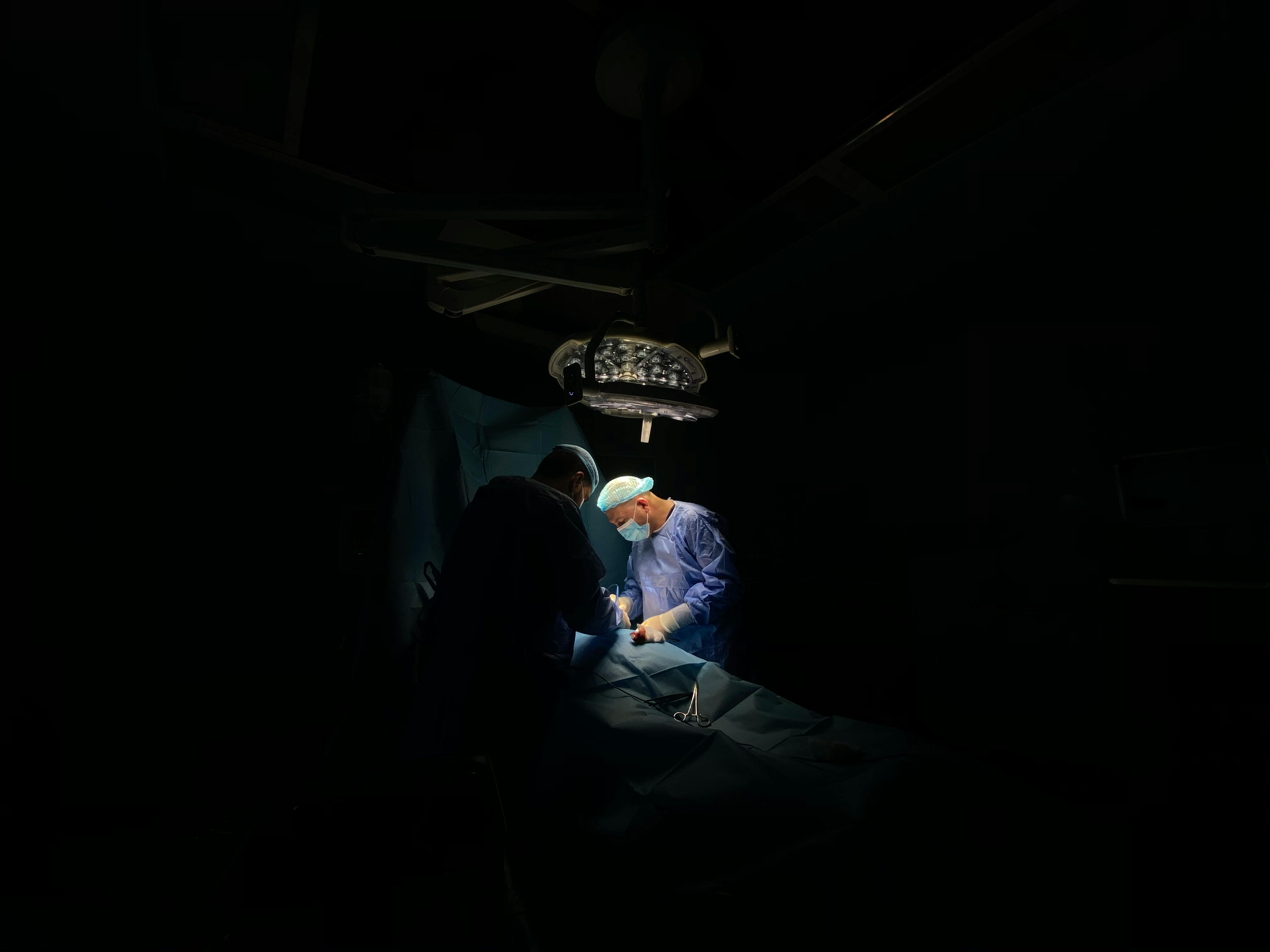 two surgeons doing surgery under a single ominous light, surrounded by darkness